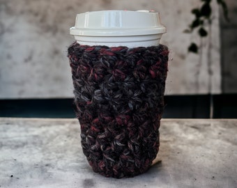 May include: A white to-go cup with a crocheted burgundy and gray sleeve.