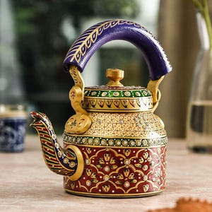 May include: A decorative teapot with a red, gold, and blue design. The teapot features intricate floral patterns, a curved handle, and a spout. The teapot is likely made of ceramic or metal and is a decorative item.