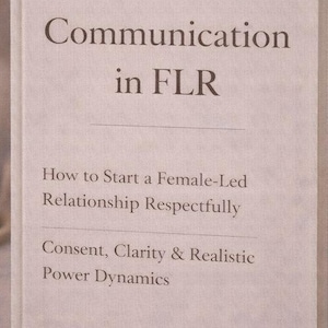 以下が含まれることがあります： 「Communication in FLR」というタイトルの本。テキストは「How to Start a Female-Led Relationship Respectfully」と「Consent, Clarity & Realistic Power Dynamics」です。本は白で、柔らかい背景、ろうそく、花瓶があります。