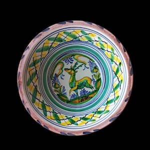 May include: A decorative ceramic bowl with a hand-painted design. The bowl features a central image of a deer in green and yellow, surrounded by blue flowers and green foliage. The rim has a brown and blue border, with green and yellow leaf patterns.