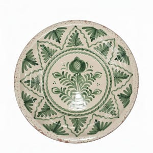 Könnte beinhalten: Ein runder, cremefarbener Keramikteller mit grünem Blumendesign. Der Teller hat ein zentrales Blumenmotiv und ein sich wiederholendes Blättermuster am Rand. Der Rand hat ein rustikales, gesprenkeltes Aussehen.