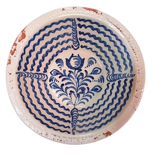Może przedstawiać: Okrągła ceramiczna miska z białym wnętrzem i niebieskim, falistym wzorem. Środek zdobi niebieski kwiatowy wzór. Obręcz ma postarzaną, czerwonobrązową powierzchnię. Ta dekoracyjna miska jest idealna do serwowania lub ekspozycji.