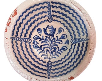 May include: A round, ceramic bowl with a white interior and a blue, wavy pattern. The center features a blue floral design. The rim has a distressed, reddish-brown finish. This decorative bowl is ideal for serving or display.