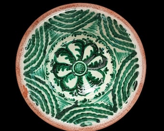 May include: Hand-painted ceramic bowl with a floral design in shades of green and white. The bowl's interior features a central flower motif and a repeating pattern around the rim. The rim is a reddish-brown color.