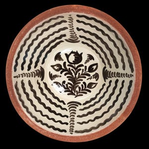 Könnte beinhalten: Eine Keramikschale mit cremefarbenem Innenraum und rotbraunem Rand. Die Schale ist mit schwarzen Wellenlinien und einem zentralen Blumendesign verziert. Das Design ist symmetrisch und die Schale ist vor schwarzem Hintergrund.