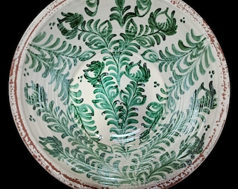 May include: A white ceramic bowl with a hand-painted green floral design. The rim has a textured, reddish-brown border. The bowl's interior features a symmetrical pattern of stylized leaves and branches.
