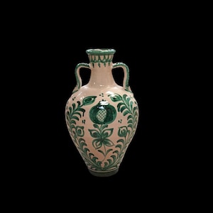 Può includere: Un vaso decorativo in ceramica con due manici, con motivi floreali e melograni verdi su una base rosa chiaro. Il vaso ha una forma arrotondata, con bordo e base verde scuro.