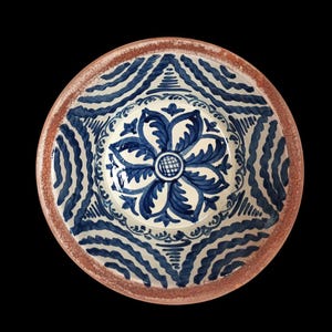 Könnte beinhalten: Eine runde Keramikschale mit floralem Design. Die Schale hat ein zentrales blaues Blumenmotiv, das von komplizierten blauen Mustern auf weißem Hintergrund umgeben ist. Der Rand ist rotbraun.
