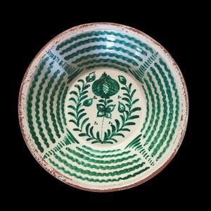 Könnte beinhalten: Eine weiße Keramikschale mit einem grün-weiß gewellten Streifenmuster am Rand. Die Mitte zeigt ein grünes Blumendesign. Die Schale hat ein rustikales, handgemaltes Aussehen und einen braunen Rand.