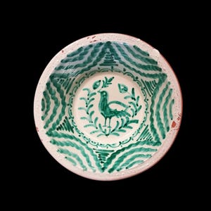 Könnte beinhalten: Eine weiße Keramikschale mit handgemaltem Design. Die Schale zeigt in der Mitte einen grünen Vogel, der von Blättern umgeben ist. Der Rand hat ein grünes Wellenmuster. Der äußere Rand der Schale ist rotbraun.