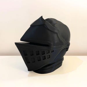 May include: A black knight helmet with a visor and a faceplate. The helmet is made of plastic and has a textured surface.