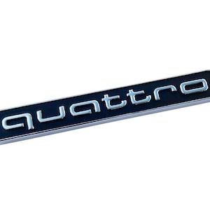May include: A rectangular black and silver emblem with the word "quattro" in silver lettering. The emblem has a silver border and is set against a white background.