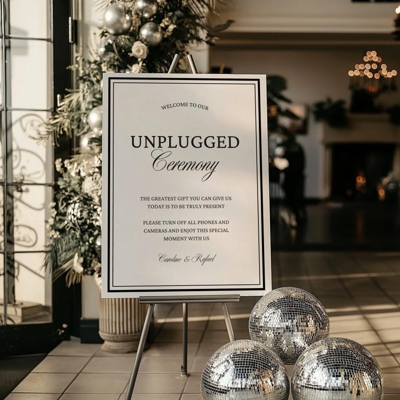 May include: A white sign on an easel with the text "Welcome to our Unplugged Ceremony." The sign is framed in black and has additional text below. Three mirrored disco balls are in front of the sign.