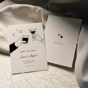 May include: Two off-white wedding announcement cards. One card features line art of hands toasting with a cocktail and wine glass, with text that reads "SAVE THE DATE" and names and date. The other card has a wine glass and cocktail glass illustration.