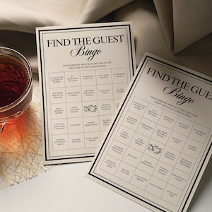 Peut inclure: Deux cartes de "Find the Guest Bingo" avec du texte noir sur fond cr&egrave;me. Les cartes ont une bordure noire et sont con&ccedil;ues pour un jeu de soci&eacute;t&eacute;. Un verre de th&eacute; est visible dans le coin.