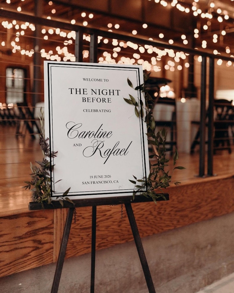 May include: A welcome sign on a black easel, announcing "The Night Before" celebrating Caroline and Rafael, with the date June 19, 2026, in San Francisco, CA. The sign is framed in black and decorated with greenery.