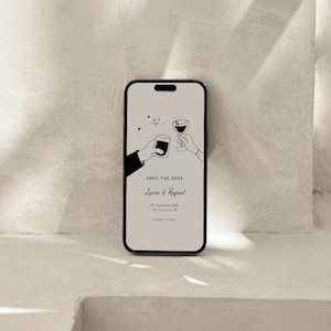 K&ouml;nnte beinhalten: Ein Smartphone zeigt eine minimalistische Hochzeitseinladung. Das Design zeigt zwei H&auml;nde, die mit einem Glas und einer Tasse ansto&szlig;en, mit Sternen und einem Mond. Der Text lautet "Save the Date" und die Namen "Liana & Rafael".