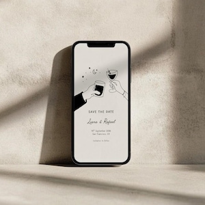 K&ouml;nnte beinhalten: Ein schwarzes Smartphone zeigt eine minimalistische Hochzeitseinladung. Das Design zeigt eine Strichzeichnung von zwei H&auml;nden, die mit einem Glas und einem Becher ansto&szlig;en, mit Sternen und einem Mond dar&uuml;ber. Der Text lautet "Save the Date" und die Namen "Liana & Rafael".