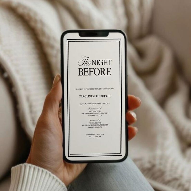 May include: A smartphone displaying a formal invitation with the text "The Night Before." The invitation is for Caroline & Theodore, with event details in black text on a white background, framed by a black border. The phone is held against a soft, neutral-toned backdrop.