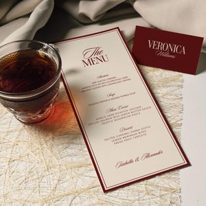 May include: A formal menu with a burgundy border and text, "The Menu," lists starters, soup, main course, and dessert options. A matching business card with the name "Veronica Williams" is also present. A glass of tea sits to the left.