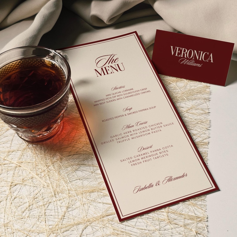 May include: A formal menu with a burgundy border and text, "The Menu," lists starters, soup, main course, and dessert options. A matching business card with the name "Veronica Williams" is also present. A glass of tea sits to the left.