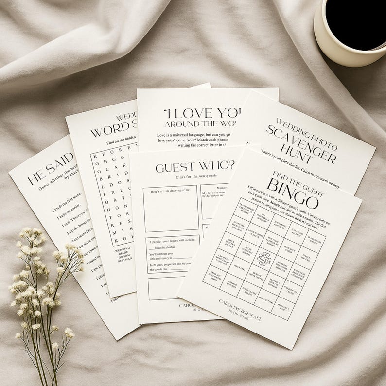 Pu&ograve; includere: Una collezione di biglietti di giochi per matrimoni bianchi con testo nero, tra cui "He Said", "Wedding Word Search", "I Love You Around the Wo", "Guest Who?", "Wedding Photo Scavenger Hunt" e "Find the Guest Bingo". Una tazza di caff&egrave; &egrave; sullo sfondo.