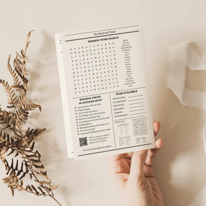 Pu&ograve; includere: Un foglio di attivit&agrave; a tema matrimonio intitolato "The Newlywed Times" con cruciverba e rompicapo. Il foglio include un codice QR e un hashtag. Una mano tiene il foglio.