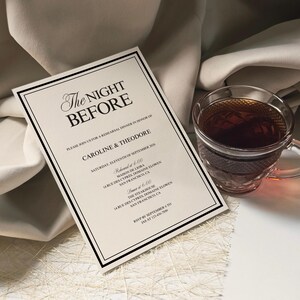 May include: A formal invitation with the text "The Night Before" in elegant script, framed with a black border. A clear glass teacup filled with tea sits beside the invitation. The invitation details a rehearsal dinner.