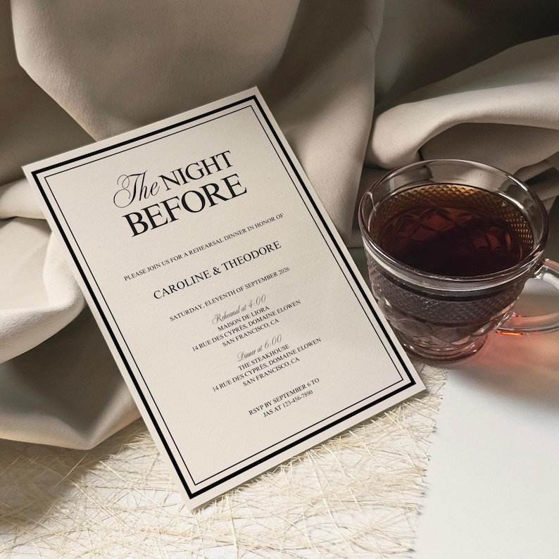 May include: A formal invitation with the text "The Night Before" in elegant script, framed with a black border. A clear glass teacup filled with tea sits beside the invitation. The invitation details a rehearsal dinner.