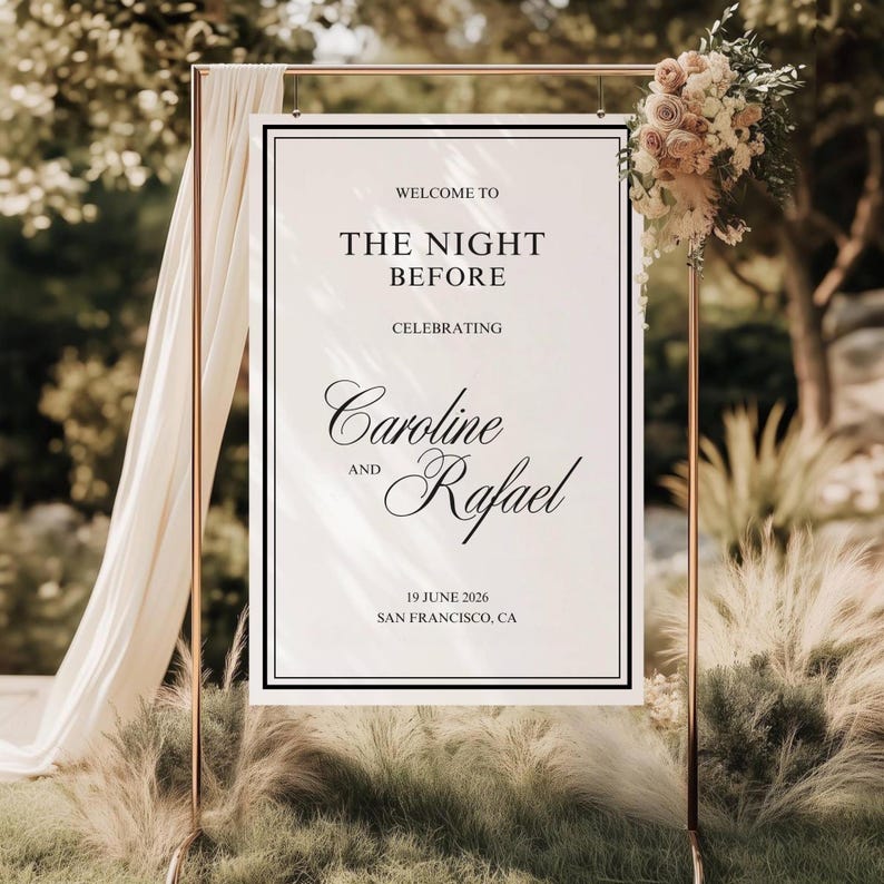 May include: A wedding welcome sign with the text "WELCOME TO THE NIGHT BEFORE CELEBRATING Caroline and Rafael 19 JUNE 2026 SAN FRANCISCO, CA." The sign is framed in black and set on a gold metal stand, adorned with flowers and draped fabric.