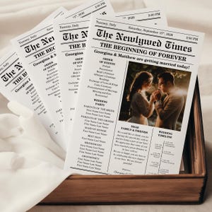 May include: A stack of wedding newspaper programs in a wooden box. The headline reads "The Newlywed Times" with the names Georgina & Matthew. The program includes the order of events, wedding party details, and a timeline.