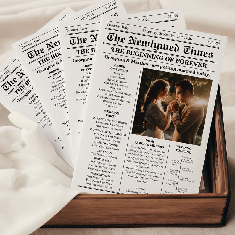 May include: A stack of wedding newspaper programs in a wooden box. The headline reads "The Newlywed Times" with the names Georgina & Matthew. The program includes the order of events, wedding party details, and a timeline.