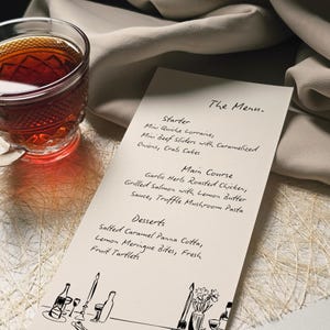 May include: A menu card with handwritten text, featuring starters, main courses, and desserts. A glass teacup with a dark liquid sits to the left. The menu includes dishes like mini quiche, roasted chicken, and salted caramel panna cotta.