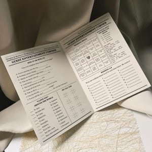 Könnte beinhalten: Offenes Hochzeitsspielheft mit Bingo, Lückentexten für Songtexte und Tic-Tac-Toe. Der Text lautet "Guest Entertainment Corner" und "Wedding Bingo". Das Heft liegt auf einer weißen Oberfläche.