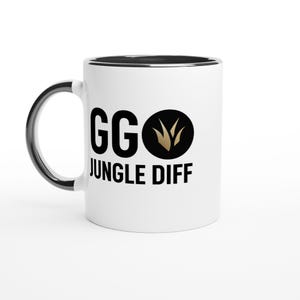 Puede incluir: Taza de cerámica blanca con asa y borde negros. La taza presenta el texto "GG JUNGLE DIFF" en negro, con un gráfico dorado y negro. La taza está diseñada para bebidas frías o calientes.