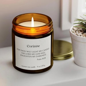 Puede incluir: Una vela de vidrio marrón con una tapa dorada. La vela está encendida y tiene un charco de cera blanca. La etiqueta dice "Corinne" e incluye el texto "FOR THOU WILT LIGHT MY CANDLE THE LORD MY GOD WILL ENLIGHTEN MY DARKNESS Psalm 18:28 coconut wax candle 9 oz | 255 g".