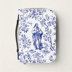 Op de afbeelding: Een wit en blauw Bijbelomslag met een toile de Jouy-ontwerp dat een figuur met een lam te midden van gebladerte afbeeldt. De hoes heeft een zwart handvat aan de zijkant.