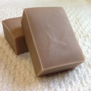May include: Two bars of handmade soap, one partially visible behind the other. The soap is a light brown color and has a smooth, slightly textured surface.