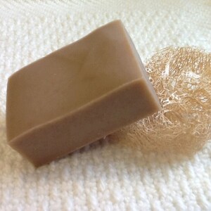 May include: A rectangular bar of brown soap, resting on a white textured surface, next to a natural loofah sponge.