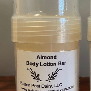 Puede incluir: Un recipiente de pl&aacute;stico blanco con una etiqueta transparente que dice "Almond Body Lotion Bar" y "Boston Post Dairy, LLC www.naturalgoatsoap.etsy.com Net Wt. .85 oz (24.1 g)".
