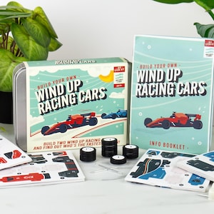 May include: A kit for building wind-up racing cars. The kit includes a tin box, an info booklet, car parts, and wheels. The box and booklet feature illustrations of red and blue race cars. The text on the box reads "Build Your Own Wind Up Racing Cars."