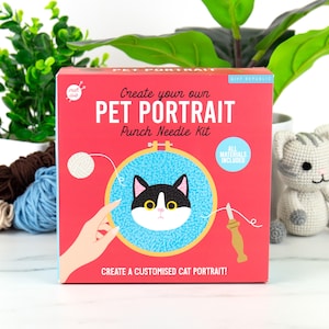 May include: A red box for a punch needle kit with the text "Create your own PET PORTRAIT". The kit includes all materials to create a customised cat portrait. The image shows a black and white cat design.