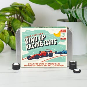May include: A DIY STEM kit for building wind-up racing cars. The kit includes a metal tin with the text "Build Your Own Wind Up Racing Cars" and illustrations of red and blue race cars. Several black and white tires are also visible.