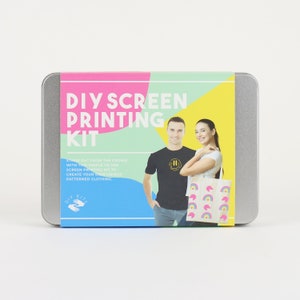Może przedstawiać: Srebrny pojemnik z kolorową etykietą z napisem "DIY Screen Printing Kit". Etykieta przedstawia mężczyznę i kobietę w koszulkach i torbie na ramię z nadrukami wykonanymi metodą sitodruku. Etykieta zawiera r&oacute;wnież tekst "Wyr&oacute;żnij się z tłumu dzięki temu łatwemu w użyciu zestawowi do sitodruku, aby stworzyć własne, niepowtarzalne ubrania z nadrukami."