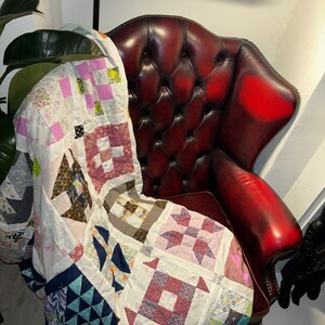 May include: A patchwork quilt featuring a variety of colours and patterns, including pink, blue, green, and brown, is draped over a red leather armchair.