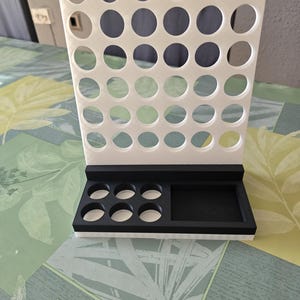 May include: A white and black organizer with multiple circular holes. The organizer has a rectangular base with several circular openings and a larger rectangular compartment. The top section features a grid of evenly spaced holes.