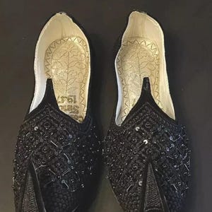 May include: A pair of black embroidered shoes with black sequins. The shoes have a pointed toe and a slip-on design.