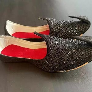 May include: A pair of black embroidered shoes with red lining. The shoes have a pointed toe and a decorative embellishment on the top.