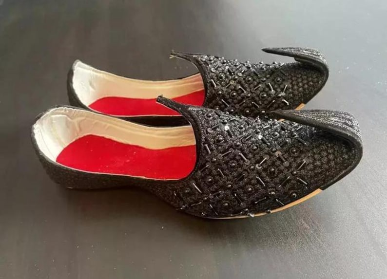 May include: A pair of black embroidered shoes with red lining. The shoes have a pointed toe and a decorative embellishment on the top.