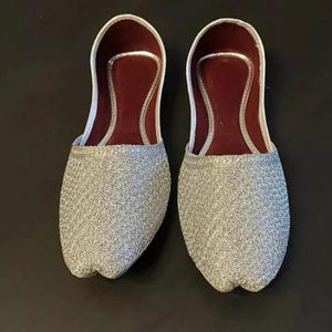May include: A pair of silver embroidered flat shoes with maroon lining.